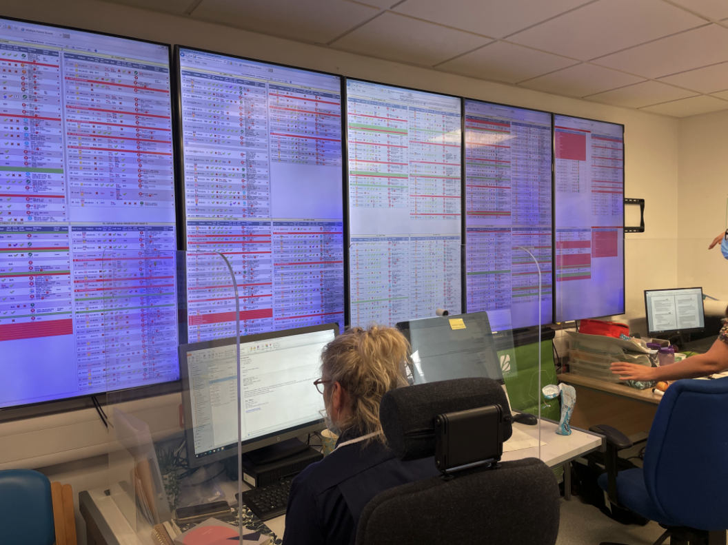 A series of five, large digital screens with a plethora of content sitting above an employee's desk